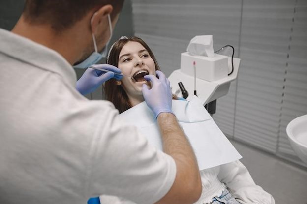 Young woman having braces tightened by orthodontist over shoulder view
