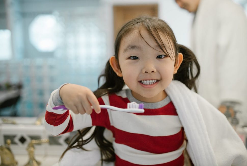 A young girl smiling while brushing their teeth